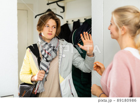 Teenage boy gesturing goodbye to mother while leaving home 89180986
