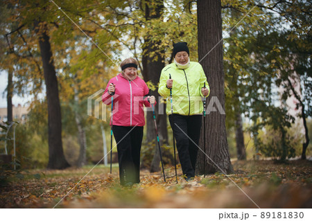 Old women walking in an autumn park during a scandinavian walk. Fall. Orange leaves Old women walking in an autumn park during a scandinavian walk. Fall. Orange leaves 89181830