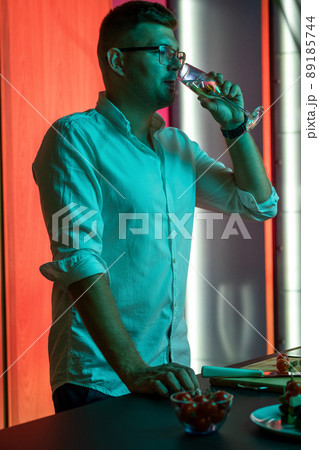 Young man enjoying glass of champagne while preparing dinner in home kitchen 89185744