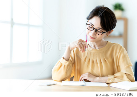 日差しが差し込む明るいリビングで勉強する眼鏡のミドル女性 89187296