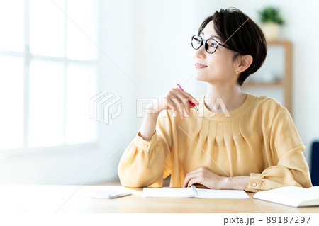 日差しが差し込む明るいリビングで勉強する眼鏡のミドル女性 日差しが差し込む明るいリビングで勉強する眼鏡のミドル女性 89187297