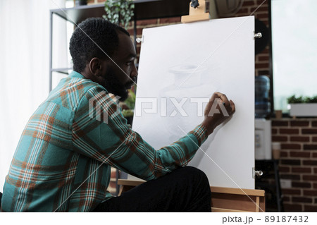 African american artist drawing vase model on white canvas working at illustration technique using graphic pencil during art lesson in creativity studio. Man sketching masterprice developing new skill African american artist drawing vase model on white canvas working at illustration technique using graphic pencil during art lesson in creativity studio. Man sketching masterprice developing new skill 89187432