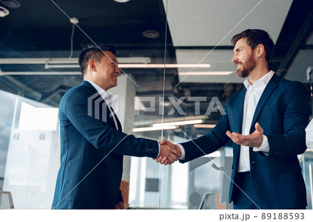 two mature diverse business partners are handshaking after successful deal in modern office two mature diverse business partners are handshaking after successful deal in modern office 89188593