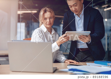 diverse mature business colleague are using tablet while working on laptop at modern office 89188596