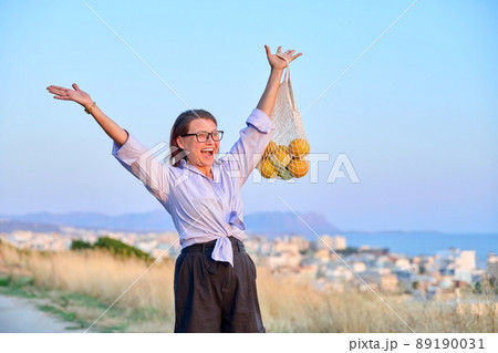 Happy joyful woman with raised hands with grid of oranges, blue sky background Happy joyful woman with raised hands with grid of oranges, blue sky background 89190031