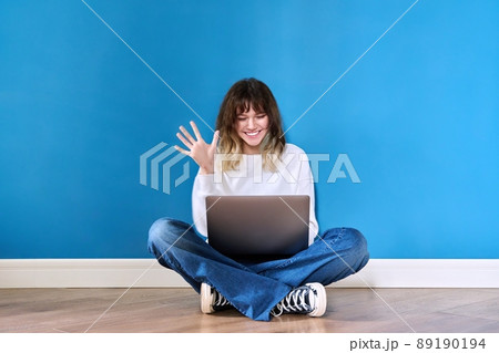 Beautiful teenage female sitting on the floor with laptop on blue background 89190194