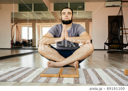 Man exercising yoga meditating sitting hands joined on the floor near sadhu board Man exercising yoga meditating sitting hands joined on the floor near sadhu board 89191100