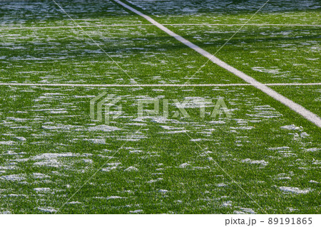 The football field with artificial green grass is covered with a light layer of snow. Early spring. 89191865