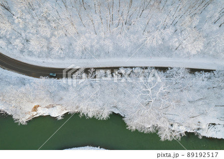 Aerial top down cinematic winter snow cowered country road, asphalt serpentine. Cars go traffic among forest. 89192517