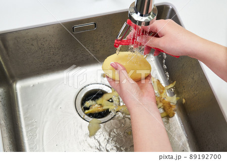 Cropped view of female hands peeling potato over Food waste disposer machine in sink in modern kitchen Cropped view of female hands peeling potato over Food waste disposer machine in sink in modern kitchen 89192700
