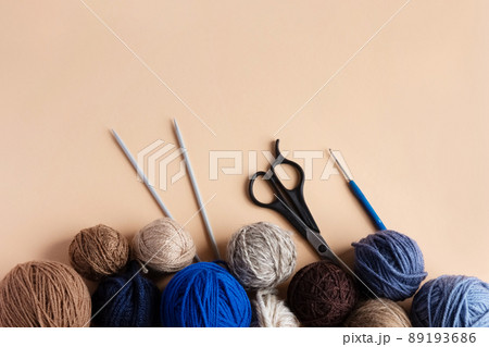 Blue, gray and brown balls of knitting thread with scissors, crochet and knitting needles on a beige background for hobbies. Flat lay 89193686