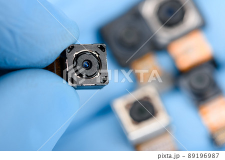 Smartphone camera module in researcher hand, with other cell phone camera sensors on background. 89196987