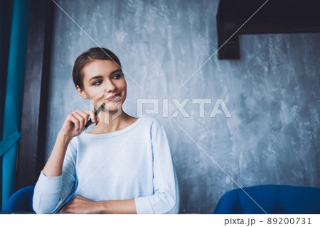 Charming pensive woman sitting at table in workspace Charming pensive woman sitting at table in workspace 89200731