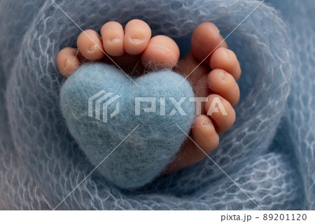 The tiny foot of a newborn baby. Soft feet of a new born in a purple, lilac wool blanket. Close up of toes, heels and feet of a newborn. Knitted purple, lilac heart in the legs of a baby.  89201120