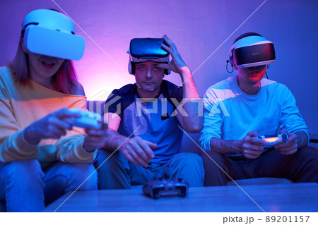 Friends playing virtual reality games using joysticks while sitting on the couch. 89201157