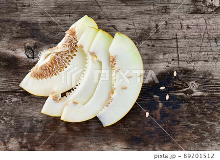 Sweet ripe melon cut on a wooden table with spilling seeds. 89201512