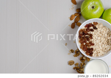 Healthy Breakfast. Oatmeal with raisins and yogurt. Milk in a glass. Fruit, nuts on a white table. Space for text 89202034