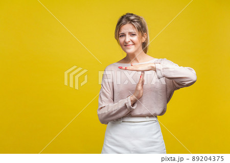 I need more time. Portrait of tired upset young woman with fair hair in casual beige blouse standing showing timeout gesture, looking at camera asking. indoor studio shot isolated on yellow background 89204375