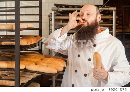 Portrait of professional adult male chef with long beard in white uniform standing in his workplace and cook with taste approval gesture, showing perfect sign. Indoor, profession concept, closed eyes 89204376