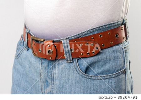 Man standing in blue jeans and brown leather handmade belt, closeup. indoor studio shot, isolated on grey background. Man standing in blue jeans and brown leather handmade belt, closeup. indoor studio shot, isolated on grey background. 89204791