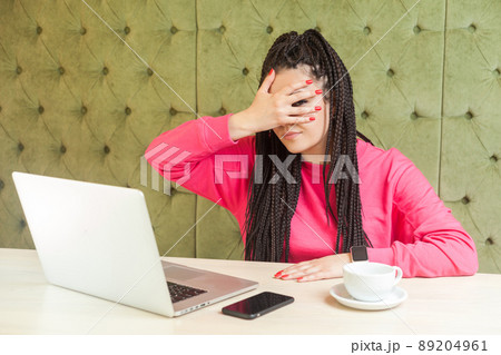 Portrait of emotional disbelief young woman with black dreadlocks hairstyle in pink blouse sitting in cafe and covering the eyes with hand, peeking cause don't want to see, looking at camera. Indoor Portrait of emotional disbelief young woman with black dreadlocks hairstyle in pink blouse sitting in cafe and covering the eyes with hand, peeking cause don't want to see, looking at camera. Indoor 89204961