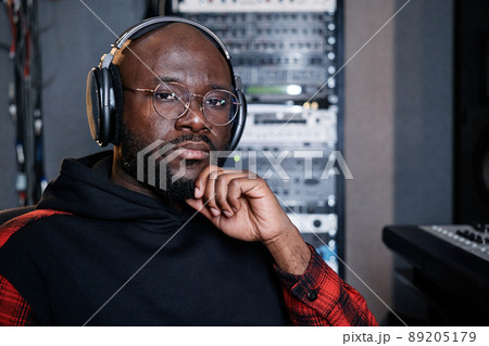 Portrait of pensive professional music producer wearing headphones sitting in recording studio looking at camera 89205179