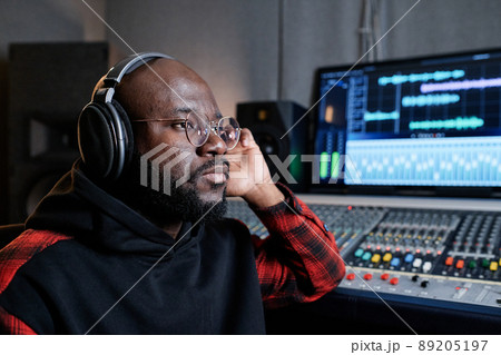 Serious mature Black music producer wearing headphones attentively listening to audio track thinking about its quality 89205197