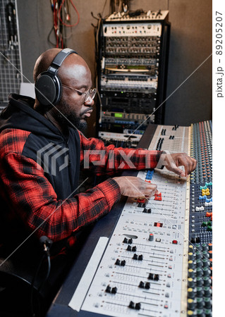 Vertical shot of modern African American male audio engineer using mixing console to create music 89205207