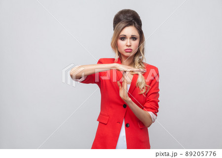 I need more time. Worry beautiful business lady with hairstyle and makeup in red fancy blazer, standing and looking at camera with timeout gesture. indoor studio shot, isolated on grey background. 89205776