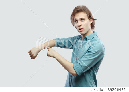 Portrait of worry handsome long haired blonde young man in blue casual shirt standing and showing time out gesture and looking looking at camera. indoor studio shot, isolated on light grey background. 89206475