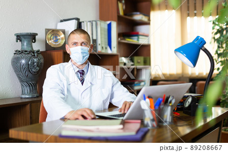 Man doctor in face mask sitting in office 89208667