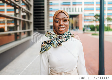 Charming black woman in Muslim headscarf standing on street Charming black woman in Muslim headscarf standing on street 89211518