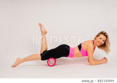 European girl is engaged in fitness on the mat. Self-massage of the muscles on a massage roller. 89216944