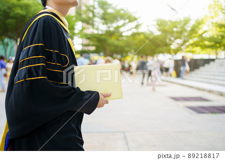 Happy Asian graduate student holding the diplomas on hand during the university graduation ceremony. Master degree student in gown suit holding a diplomas for photography. 89218817