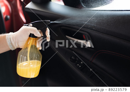 Unrecognizable man spraying a cleaning solution or liquid sanitizer on a the surface of door panel in a car. Vehicle garage and car care service concept. 89223579