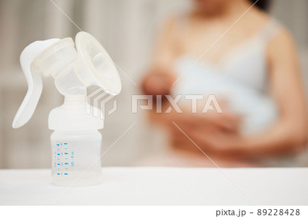 breast pump with breast milk against the background of a mother holding child. breast pump with breast milk against the background of a mother holding child. 89228428