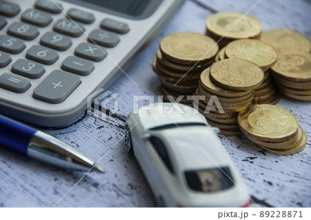 Gold coins, calculator, white car toy and pen on wooden background. Selective focus on coins. Business concept Gold coins, calculator, white car toy and pen on wooden background. Selective focus on coins. Business concept 89228871