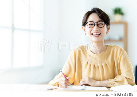 日差しが差し込む明るいリビングで勉強する眼鏡のミドル女性 89233289