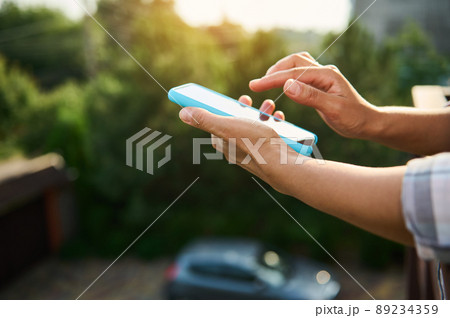 Close-up of woman hands holding mobile phone against sunlight background 89234359