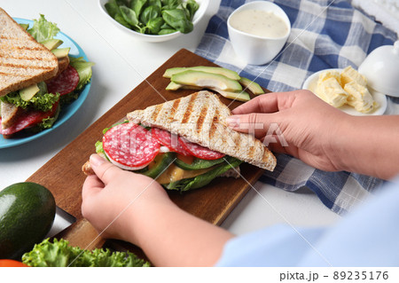 Woman making tasty sandwich with sausage at white table, closeup Woman making tasty sandwich with sausage at white table, closeup 89235176