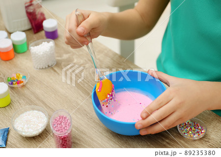 Little girl mixing ingredients with silicone spatula at table, closeup. DIY slime toy Little girl mixing ingredients with silicone spatula at table, closeup. DIY slime toy 89235380