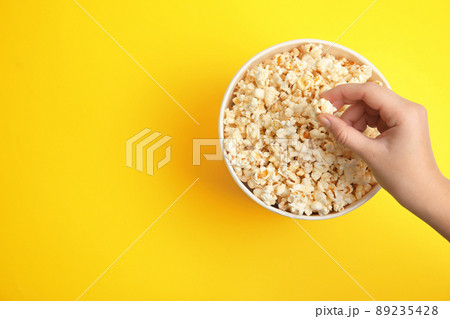Woman taking fresh pop corn from bucket on yellow background, top view. Space for text Woman taking fresh pop corn from bucket on yellow background, top view. Space for text 89235428