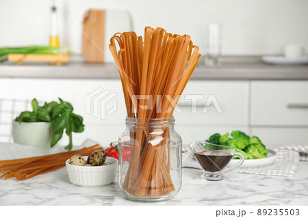 Uncooked buckwheat noodles and fresh ingredients  on white marble table in kitchen 89235503