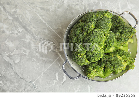 Fresh green broccoli in colander on grey marble table, top view. Space for text 89235558