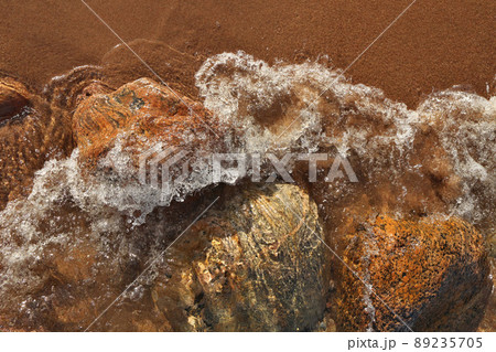 Directly Above Shot of Small Waves Rolling into Beach Dotted with Colorful Rocks and Boulders Directly Above Shot of Small Waves Rolling into Beach Dotted with Colorful Rocks and Boulders 89235705