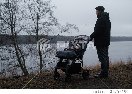 Grandfather walking with a baby stroller on cold and gloomy spring day Grandfather walking with a baby stroller on cold and gloomy spring day 89252590