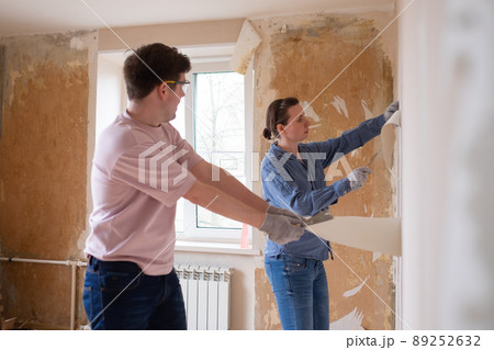 Young couple removing old wallpaper from walls preparing for flat renovation. Young couple removing old wallpaper from walls preparing for flat renovation. 89252632