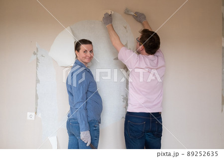 Young couple removing old wallpaper from walls preparing for flat renovation. 89252635
