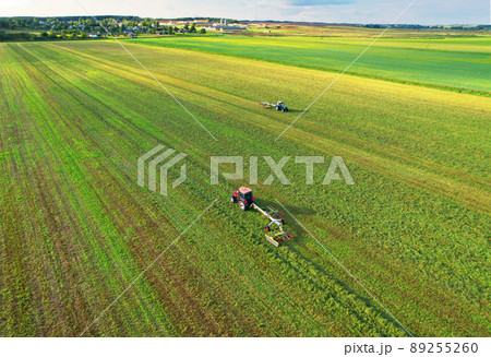 Tractor raking grass for silage harvesting. Agriculture farm machinery work at field. Tractor raking grass for silage harvesting. Agriculture farm machinery work at field. 89255260