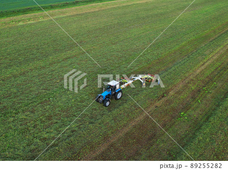 Tractor raking grass for silage harvesting. Agriculture farm machinery work at field. 89255282